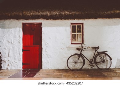 Traditional irish thatched cottage, with red wooden two parts door and an old bicycle. Artistic washed out faded vintage retro edit. - Powered by Shutterstock