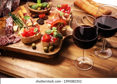 Traditional italian antipasto bruschetta appetizer with cherry tomatoes, cream cheese, basil leaves and balsamic vinegar on cutting board with prosciutto, salami, cheese,bread and olives