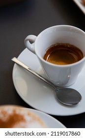 Traditional Italian Breakfast. Small White Ceramic Cups With Espresso (coffee) On A Table With A Saucer And A Metal Spoon At A Local Bar (coffee Shop) In Milan, Lombardy, Italy. European Drinks.