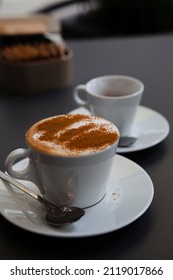 Traditional Italian Breakfast. Small White Ceramic Cups With Espresso Coffee And Cappuccino On A Table With Saucers And Metal Spoons At A Local Bar (European Coffee Shop) In Milan, Lombardy, Italy. 