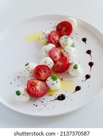 Traditional Italian caprese salad on a white plate close-up. Mini mozzarella and cherry tomatoes salad with herbs and balsamic