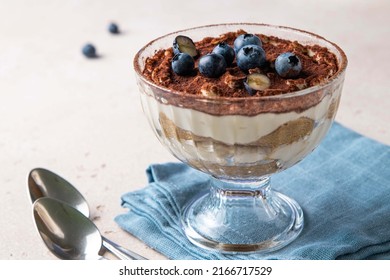 Traditional Italian dessert tiramisu with blueberries in glass. Individual homemade layered cake with berries in cup. Selective focus.