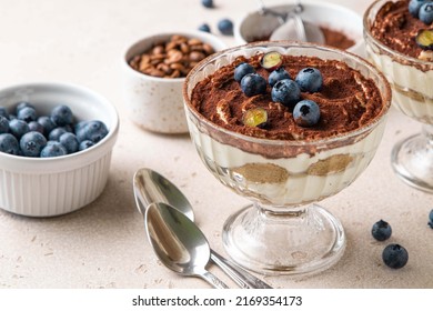 Traditional Italian dessert tiramisu with blueberries in glass. Individual trifle. Homemade layered cake with berries in cup. Selective focus.