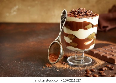 Traditional italian dessert tiramisu with chocolate sauce in a glass on a dark rustic slate, stone or concrete background.