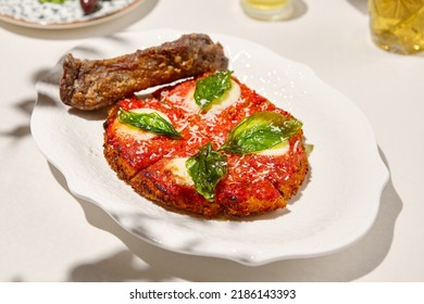 Traditional Italian Dish - Milanese Steak In Breaded And Parmesan On White Ceramic Plate. Milanese Beef With Tomato Sauce And Basil. Italian Beef Steak Alla Schnitzel With Bone. Italian Chop Beef