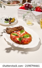 Traditional Italian Dish - Milanese Steak In Breaded And Parmesan On White Ceramic Plate. Milanese Beef With Tomato Sauce And Basil. Italian Beef Steak Alla Schnitzel With Bone. Italian Chop Beef