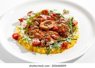 Traditional Italian dish - osso buco with risotto Milanese and cherry tomato and rucola. Ossobuco with saffron rice isolated on white background. Stewed meat on bone with yellow risotto