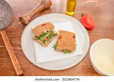 Traditional Italian Focaccia Recipe With Arugula, Cheese And Dried Tomato On A White Plate And With A Pepper Shaker, Grated Parmesan Cheese And Olive Oil.