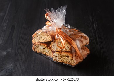 Traditional Italian food. Sweet biscuits cantuccini with almonds. Wrapped in a package with a bow. Dark background