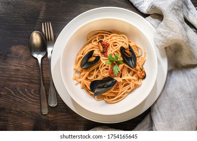 Traditional Italian Lunch Spaghetti With Mussels In Tomato Sauce On Wooden Table. Food Italy Capri Rome Sicily Sardinia. Seafood Recipe. Selective Focus Top View.  Restaurant  Food Delivery