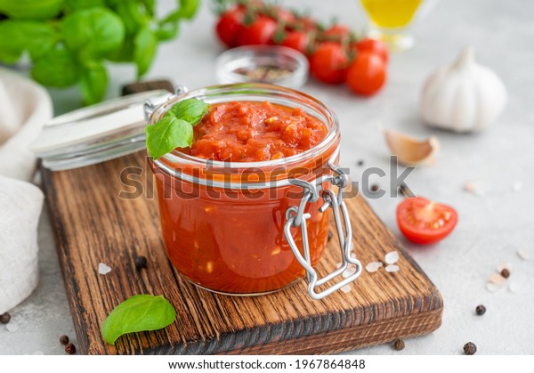 Traditional Italian\
marinara sauce in a jar on a concrete background with spices and\
ingredients. Copy\
space