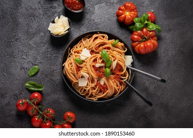 Traditional Italian pasta with tomato sauce, basil and cheese on the black background, top down view with copy space
