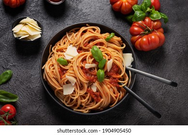 Traditional Italian pasta with tomato sauce, basil and cheese on the black background, top down view with copy space