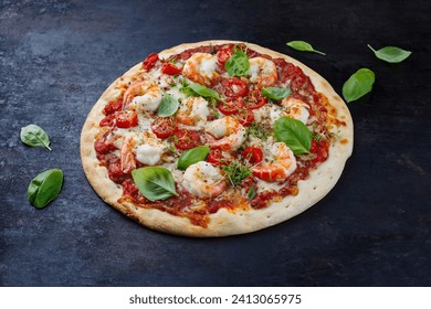 Traditional Italian pizza frutti di mare with king prawns, tomatoes and mozzarella served as close-up on a rustic black board
