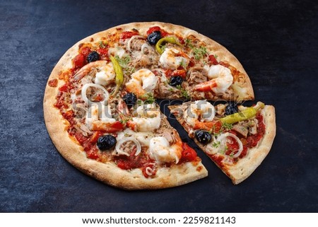 Traditional Italian pizza frutti di mare with king prawns, tuna and olives served as close-up on a rustic black board