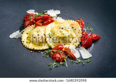 Traditional Italian ravioli pasta offered with parmesan cheese and fried tomatoes as closeup on a modern design plate 