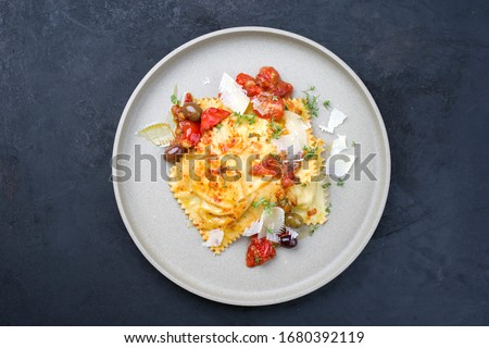 Traditional Italian ravioli pasta offered with parmesan cheese, fried tomatoes and olives as top view on a modern design plate with copy space 