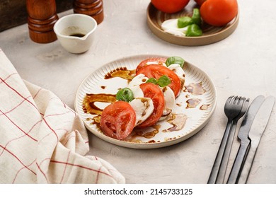 Traditional italian salad caprese consisting of slices red tomatoes, fresh basil and mozzarella cheese with balsamic vinegar dressing on concrete background, wooden pepper and salt mills