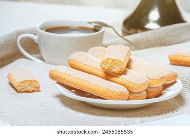 Traditional italian savoiardi biscuits or ladyfingers cookies on a plate and white cup of coffee on background. Selective focus - Powered by Shutterstock