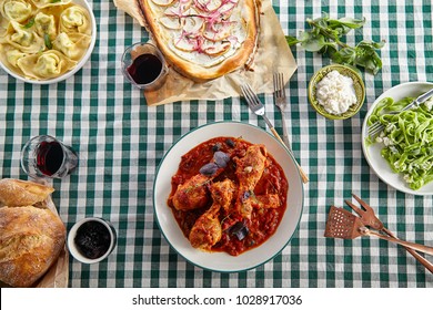 Traditional Italian Tuscan Family Dinner With Homemade Pasta And Chicken Cacciatore, Focaccia And Salad Served On A Table Covered With Green Checkered Tablecloth