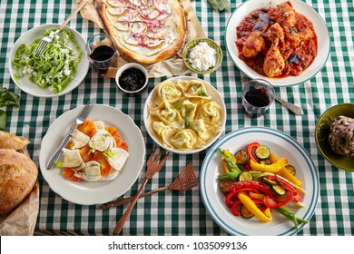 Traditional Italian Tuscan Family Dinner With Homemade Pasta And Chicken Cacciatore, Focaccia And Salad Served On A Table Covered With Green Checkered Tablecloth