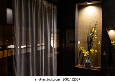 Traditional Japanese House Or Ryokan Home Hotel With Yellow Flower Ikebana In Vase Decoration Decor Illuminated By Lamp In Dark Room With Curtains At Night