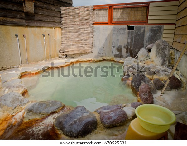 Traditional\
Japanese open air hot spring bath: Beppu, Kyushu, Japan - April 25,\
2017: Plastic bucket by a family hot spring bath with natural\
sulfurous water flowing out from the\
grounds.