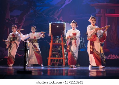 Traditional Japanese Performance. Group Of Actresses In Traditional White And Red Kimono And Fox Masks Dance And Drum A Big Taiko Drum On The Stage.