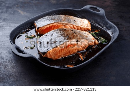 Traditional Japanese salmon fish teriyaki filet with soy souce and spinach as close-up in a Nordic design pan