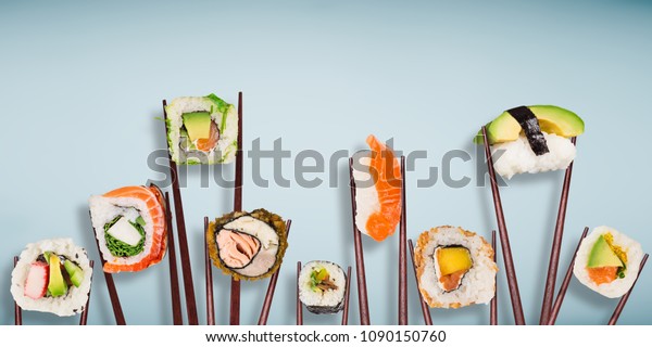 Traditional japanese sushi pieces placed between\
chopsticks, separated on light blue pastel background. Very high\
resolution image.