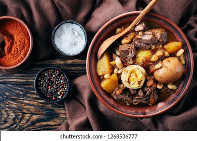 Traditional Jewish Cholent Hamin - main dish for the Shabbat meal, slow cooked beef with potato, beans and brown eggs in a bowl on a rustic wooden table, view from above, flatlay