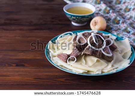 traditional Kazakh Asian dish Beshbarmak: noodles with lamb and onions close-up on a plate on the table. near the broth in bowls. dastarkhan.