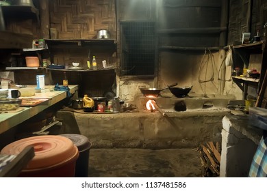 Traditional Kitchen In Old Nepali House In Small Remote Village In Himalayas With Open Fire Place, Smoking Coal, Kettles, Frying Pans And Pots. Interior Of A Poor Asian House.