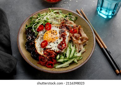 Traditional Korean dish Bibimbap. Bowl with rice, shiitake mushrooms, chicken, cucumber and microgreens and Korean bibimbap sauce. Dark background, copy space for text
