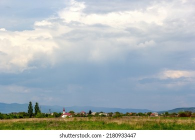 Traditional landscape of Transcarpathia. A church is visible on the horizon, and behind it are mountains. Cloudy spring sky, afternoon. Selective focus, place for text. Transcarpathia, Ukraine, Europe