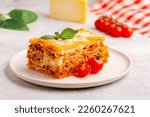Traditional lasagna with bolognese sauce topped with basil leaves served on a white plate