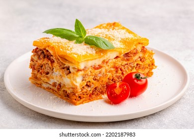 Traditional lasagna with bolognese sauce topped with basil leaves served on a white plate - Shutterstock ID 2202187983