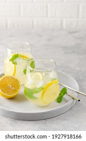 Traditional lemonade with lemon, mint and ice in a glass with metal straw on a gray concrete background. Refreshment summer drink. Copy space