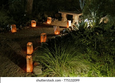 Traditional Luminarias Or Farolitos Lighting A Path To A Stone Bench In A Garden