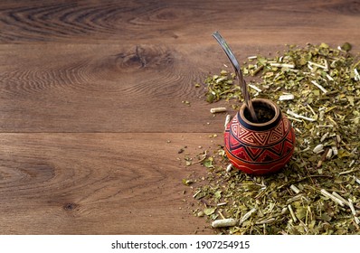 Traditional mate made of calabash over a wooden table with yerba mate scattered over it.