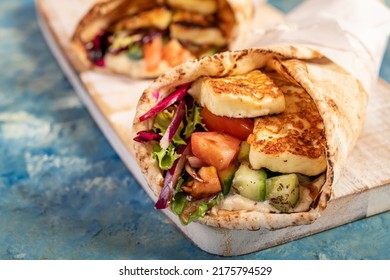 Traditional Mediterranean Arabic Grilled Halloumi, Hummus And Vegetables In Flatbread Wraps Topped With Herbs And Balsamic Vinegar On Blue Background