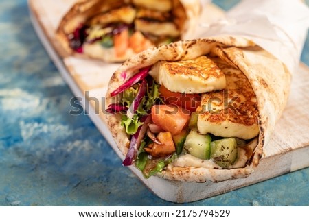 Traditional Mediterranean Arabic grilled halloumi, hummus and vegetables in flatbread wraps topped with herbs and balsamic vinegar on blue background
