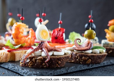 Traditional Mediterranean sandwiches - Spanish tapas consisting of octopus with tentacles, quail egg, green olive, cream cheese - side view of a set of tapas in the bar
