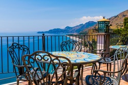 Traditional Mediterranean Seaside Restaurant On The Hillside With Mosaic Deacorated Wrought Iron Tables And Chairs And Amazing Blue Sea Panorama With Clear Blue Sky, Sicily