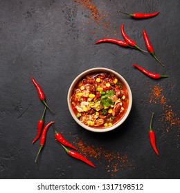 Traditional Mexican Dish Chili Con Carne In Ceramic Bowl On Black Concrete Background With Chili Peppers. Overhead View, Flat Lay, Copy Space. Minimal Abstract Composition