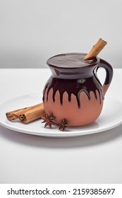 Traditional Mexican Drink Based On Corn And Chocolate Served In A Clay Cup Accompanied By Cinnamon And Anise On A White Background, No People