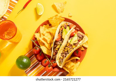 Traditional Mexican food corn tacos with meat, vegetables, avocado, beans, corn, salsa and nachos. Served with various sauces and drinks on yellow background. Top view. Big family gatherings.