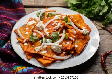 Traditional mexican food. Red chilaquiles with cheese and sour cream on wooden background