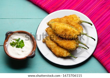 Traditional mexican jalapeno poppers stuffed with cheese and breaded on turquoise background