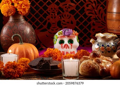 Traditional Mexican offering for the Day of the dead with a sugar skull, bread of the dead, Aztec marigold (Spanish: Cempasuchil), pumpkin, chocolate and candles. Typical cut paper on the background. - Shutterstock ID 2059876379